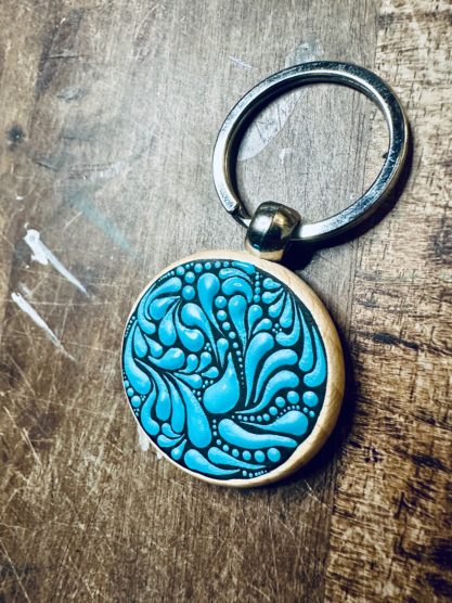 Türkisfarbener Schlüsselanhänger mit kunstvollen, gewundenen Mustern.